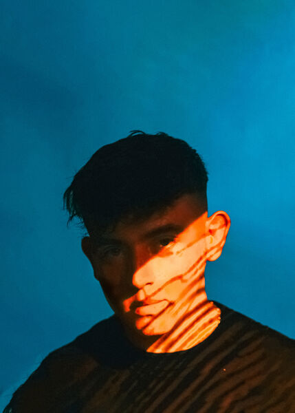 Modeā, 2026 press photo: cyan backdrop with orange striped light across his face