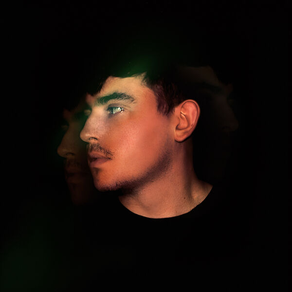 Modeā, moody double-exposure profile on black with a green flare